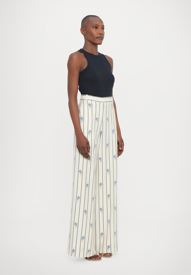 Black sleeveless top paired with high-waisted white striped pants featuring blue floral patterns and vertical lines. Fabric has a smooth texture.