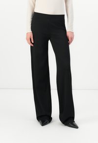 Black wide-leg trousers made of smooth fabric, featuring a high waistband and subtle side seams. Paired with pointed black shoes.