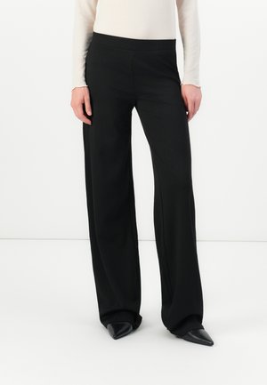 Pantalons noirs à jambes larges en tissu lisse, dotés d'une taille haute et de coutures latérales discrètes. Associés à des chaussures noires à bouts pointus.
