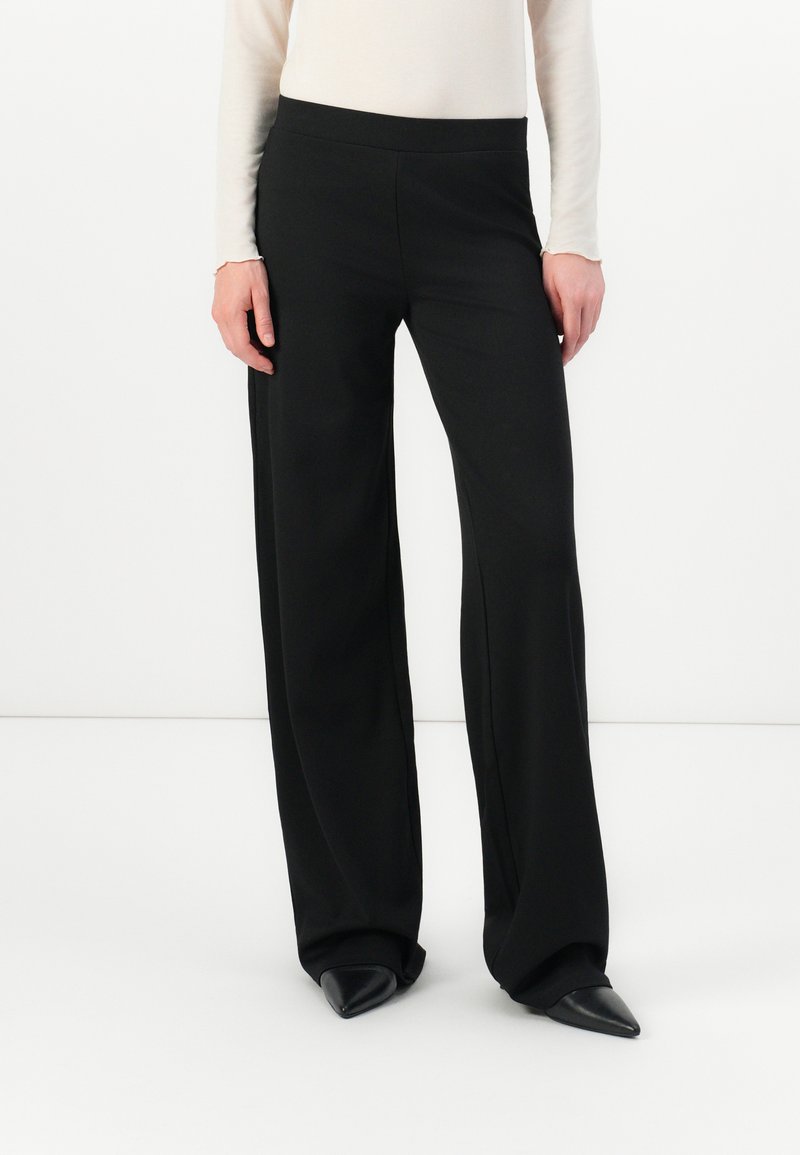 Black wide-leg trousers made of smooth fabric, featuring a high waistband and subtle side seams. Paired with pointed black shoes.