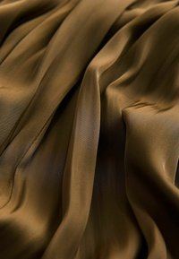 Tissu brun, soyeux avec une texture douce, comportant des drapés souples et des plis doux. La surface a un éclat subtil et une légère variation de couleur.