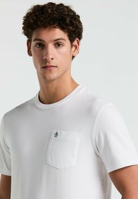 Witte t-shirt met korte mouwen van gladde stof. Heeft een borstzak met een klein pinguïnlogo. Eenvoudig en klassiek ontwerp.