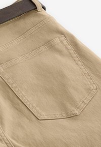 Beige katoenen broeken met een zichtbare achterzak, voorzien van stiksels en een gladde textuur. Inclusief een bruine leren ceintuurlus.