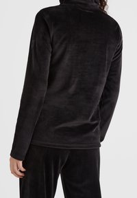 Pullover de felpa negra con collar alto, mangas largas y una textura suave y lisa. Etiqueta notable en la manga izquierda.