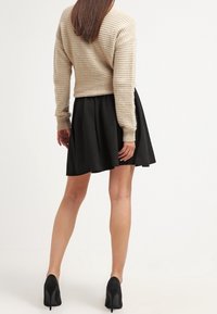 Beige ribbaettu crop-svettari yhdistetty mustaan flared-hameeseen. Mustat korkokengät viimeistelevät asun. Tasainen rakenne ja istuva muotoilu.