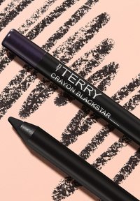 Eyeliner neri a matita sono esposti su uno sfondo pesca, con un cappuccio viola scintillante e un marchio raffinato. Le texture notevoli includono una finitura liscia.