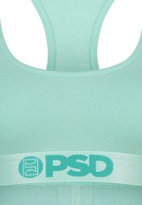 Svetlofialová športová podprsenka so zaobleným výstrihom a širokým pásom s kontrastným logom "PSD" v mierne tmavšej fialovej. Mäkká, elastická látka.
