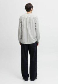 Lichtgrijze langjarig shirt met een ronde zoom, knoopmanchetten en een geplooid rugdetail, gecombineerd met zwarte wijde broek.