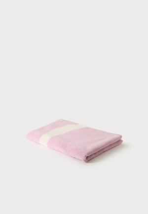 Serviette rose pliée avec une bande diagonale blanche sur un fond blanc uni.