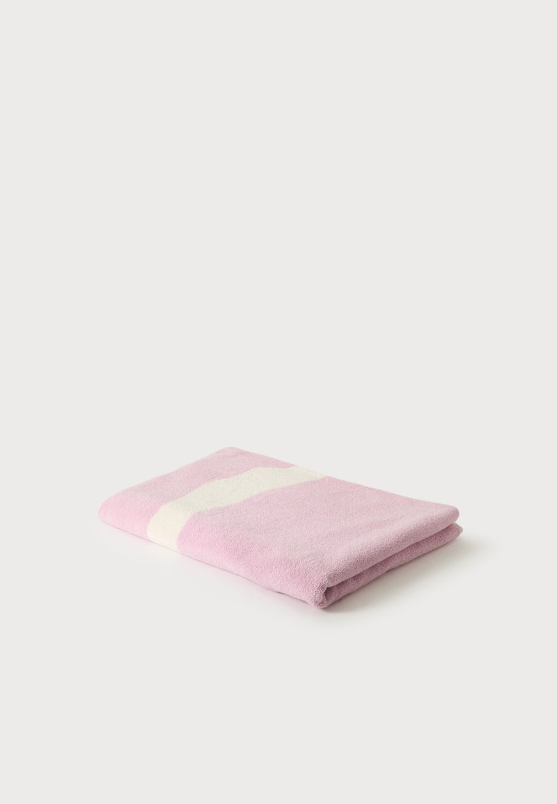 Serviette rose pliée avec une bande diagonale blanche sur un fond blanc uni.