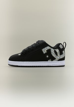 Scarpa da ginnastica nera a taglio basso con logo DC a stampa leopardata sul lato, lacci neri, suola bianca e anello di presa sul tallone.