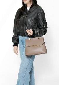 Giacca bomber in pelle grigia, jeans blu chiaro, tiene una borsa beige con chiusura e accenti dorati, forma strutturata, texture liscia.