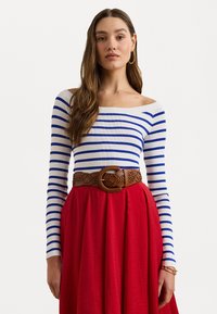 Balta off-the-shoulder palaidinė su mėlynomis juostelėmis, derinama su raudona sijonu ir nertuoju ruduo diržu su dideliu apvaliu užsegimu.