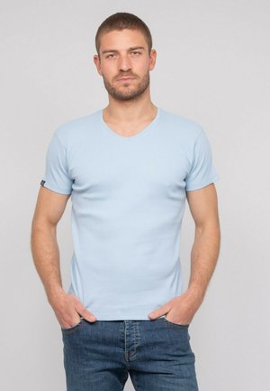 T-shirt bleu clair à manches courtes et col en V, fabriqué en tissu côtelé. Design ajusté avec une texture subtile, associé à un jean en denim noir.