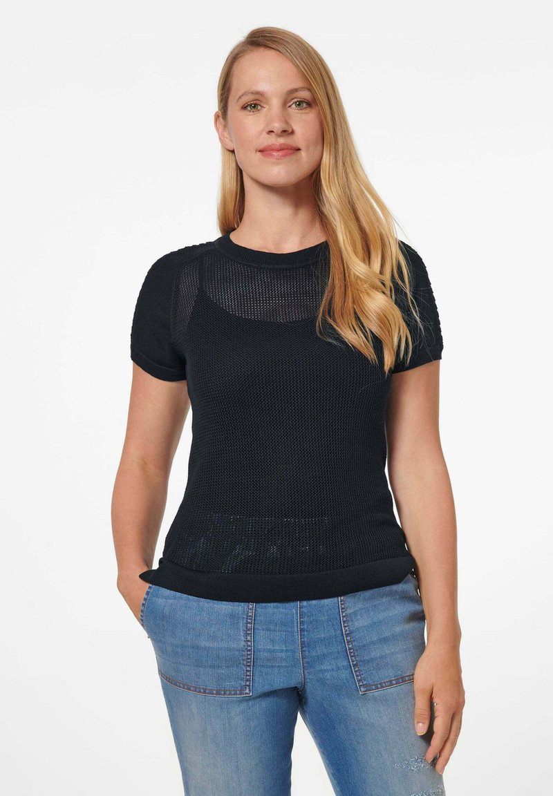 Schwarzes kurzärmliges Strickoberteil mit strukturiertem Muster, Rundhalsausschnitt und geripptem Saum. Kombination mit hellblauen Jeans.