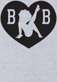 La tela gris presenta una forma de corazón negro con la silueta blanca de una persona en una pose y la letra "B" a cada lado.