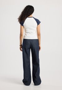 Camiseta de raglán blanca y marina con mangas cortas, combinada con pantalones de pierna ancha de rayas oscuras, que muestran un ajuste relajado y una tela texturada.