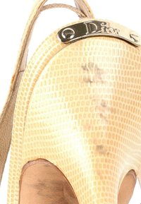 Gros plan d'une chaussure beige texturée Christian Dior avec de petites boucles et une plaque logo métallique sur la bride arrière.
