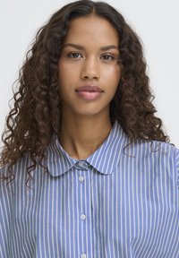 Blå og hvidstribet skjorte med knapper foran og rund krave, fremstillet i glat stof med seks matchende knapper ned langs fronten.