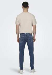 Camiseta de rayas beige con mangas cortas, combinada con jeans azul oscuro que tienen bolsillos traseros y una etiqueta marrón en la cinturilla.