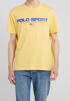 Żółta bawełniana koszulka z krótkim rękawem, z niebieskim napisem "POLO SPORT", czerwonym napisem "RALPH LAUREN" oraz małą grafiką amerykańskiej flagi.