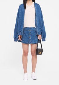 Jeansová bomber bunda s žebrovanými manžetami, světlá béžová polo tričko, sukně z jeanu s vysokým pasem a předními knoflíky, černá kabelka, bílé tenisky.