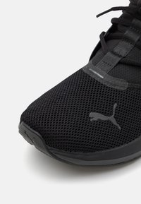 Černá sportovní bota s textilním svrškem, zakulacenou špičkou a texturovanou podrážkou. Výrazné černé logo Puma na boku a středový systém šněrování.