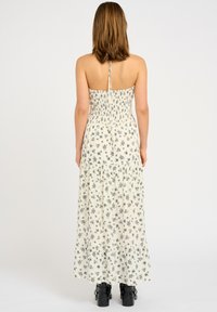 Rochie maxi cu o bustă ajustată și textură plisată, având modele florale negre pe un fundal crem și o margine cu volane.