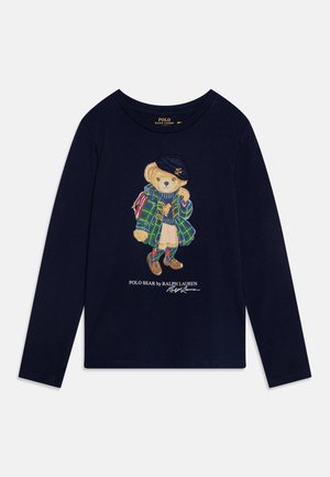 Marineblaues Langarmshirt mit einem Bären, der einen karierten Mantel, eine Baskenmütze, einen Pullover, einen Rock und Stiefel trägt, sowie dem Text "Polo Bear by Ralph Lauren" darunter.