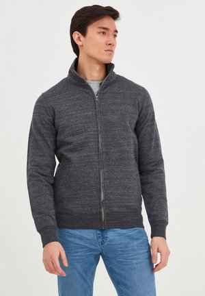 Donkergrijze zip-up jack met een gestructureerde stof, hoge kraag en zijzakken. Gecombineerd met lichtblauwe jeans voor een casual look.