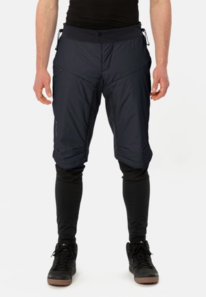 Shorts rembourrés noirs avec des jambes fuselées, une taille élastique et des poches zippées. Superposés sur des leggings noirs ajustés. Finition texturée.