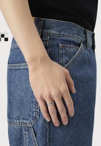 Hand with silver ring resting beside a person wearing blue denim jeans and a black top.