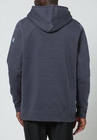 Sudadera con capucha de color gris oscuro y textura suave. Presenta puños y dobladillo acanalados, y un logo bordado en el hombro izquierdo.