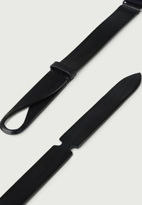 Porta coltelli in pelle nera con manico ad anello, dotato di una lama sottile. Il design è elegante, con una superficie liscia e una forma minimalista.