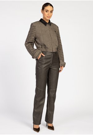 Gekürzte Jacke mit strukturiertem grauen Körper und schwarzem Lederkragen, kombiniert mit hochgeschnittenen schwarzen Lederhosen. Spitzer Absatzschuhe runden den Look ab.