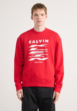Rode sweatshirt met lange mouwen, voorzien van een witte grafische ontwerp en de woorden "CALVIN" en "Calvin Klein" gedrukt op de voorkant.