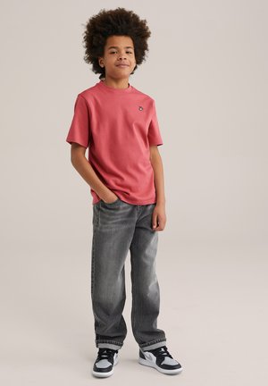 Rode katoen t-shirt met korte mouwen en een klein zwart logo. Draagt met vervaagde grijze jeans en zwart-witte sport sneakers.