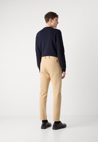 Námornícky sveter a béžové nohavice z bavlneného zmesi. Nohavice majú zadnú kapsu a malé detaily loga. Čierne topánky dotvárajú outfit.