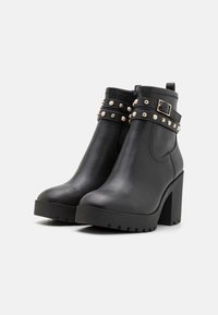 Cizme negre de gleznă din piele, cu un toc chunky, având accente cu studuri și un design cu curea. Talpă texturată pentru aderență.
