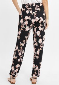 Pantaloni floreali neri in tessuto morbido, con vita elastica e un motivo di fiori rosa e bianchi con dettagli verdi.