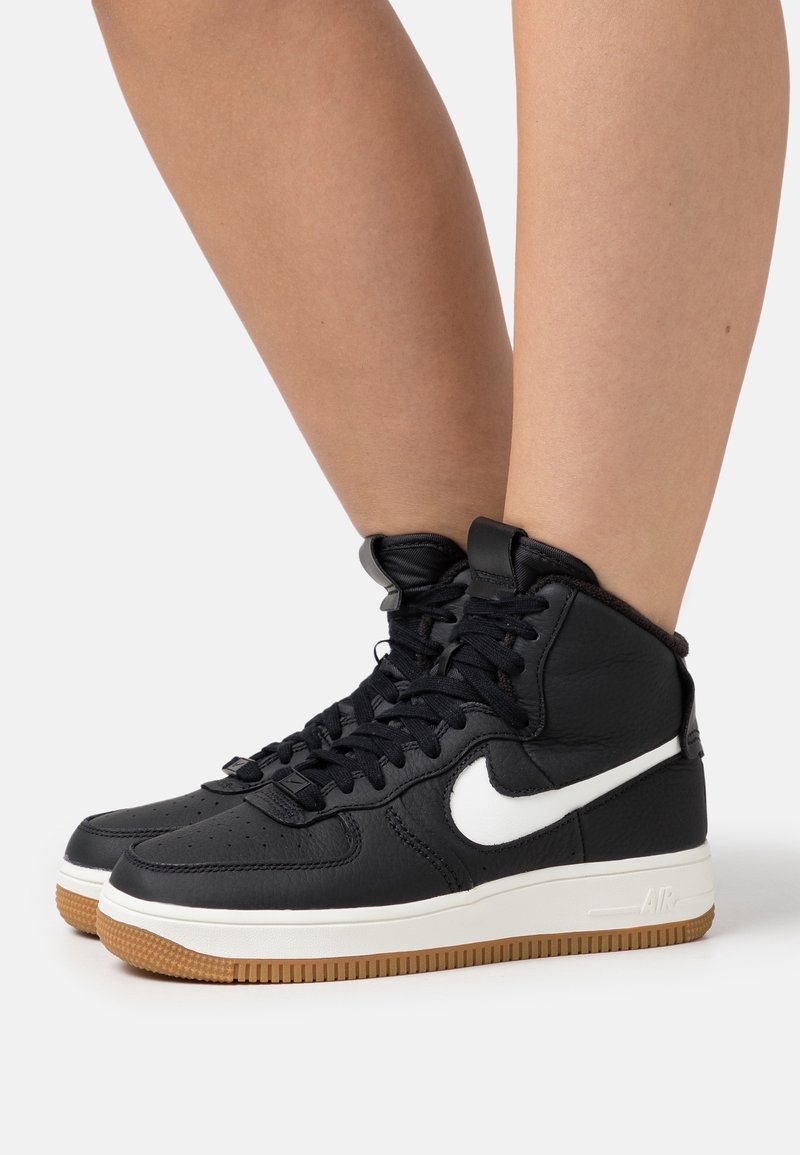 Svarta läder hög-top sneakers med vit Nike swoosh, svarta snörningar och gummisulor. Har vadderad krage för stöd vid anklarna.