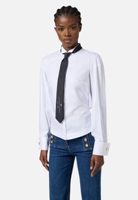 Camicia bianca a maniche lunghe con cravatta nera con testo; jeans blu con bottoni dorati; tessuto morbido; vestibilità su misura.