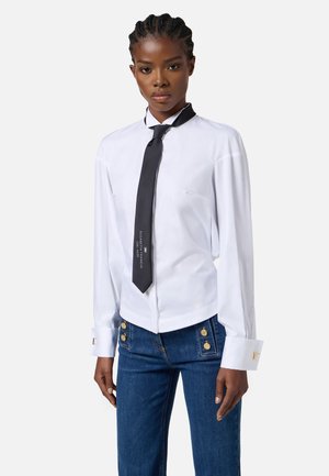 Camicia bianca a maniche lunghe con cravatta nera con testo; jeans blu con bottoni dorati; tessuto morbido; vestibilità su misura.