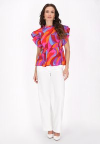 Top peplum colorat în nuanțe de roz, portocaliu și albastru, cu mâneci bufante, asortat cu pantaloni largi albi și pantofi albi cu toc.