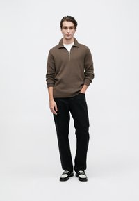 Sudadera marrón con cremallera y cuello acanalado, combinada con pantalones negros y zapatos negros con detalles en blanco. Tejido texturizado, ajuste casual.