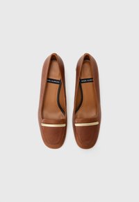 Brown leather flats featuring a smooth texture, rounded toe, and a gold-tone metal accent across the vamp. Black inner lining.