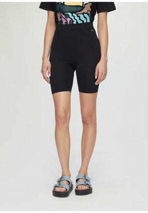 Shorts de vélo noirs à taille haute, texture lisse, associés à des sandales bleues avec des sangles à boucle et une semelle épaisse.