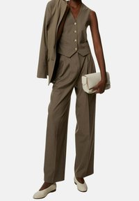 Brązowy, trzyczęściowy garnitur w prążki z bezrękawnikiem i szerokimi spodniami, zestawiony z białą kopertówką i plecionymi beżowymi butami.