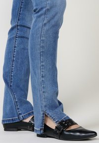 Siniset farkut, joissa on suora leikkaus ja sivurei'ät helmassa. Yhdistetty mustiin tennarikenkiin, joissa on metalliset niitit ja hihnat.