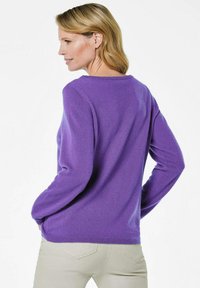 Lila gestrickter Pullover mit langen Ärmeln und rundem Ausschnitt. Hat eine weiche Textur und eine gerade Passform, kombiniert mit hellen Hosen.
